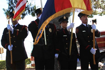 four fire fighters in formal uniform holding flags and axes